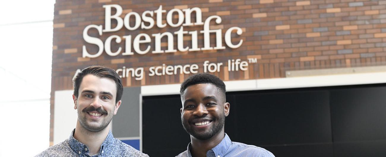 Two men in front of Boston Scientific logo on office wall 